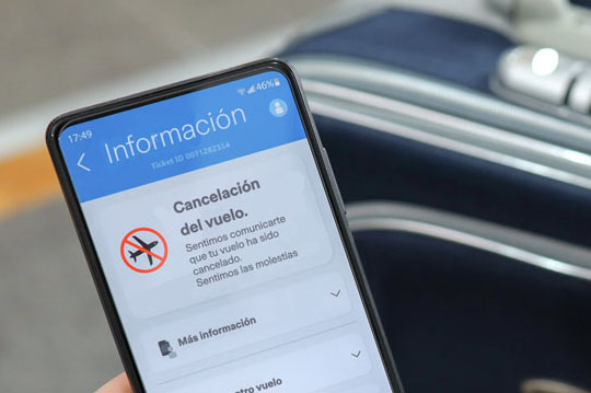 Móvil mostrando información sobre la cancelación de un vuelo con maleta de fondo