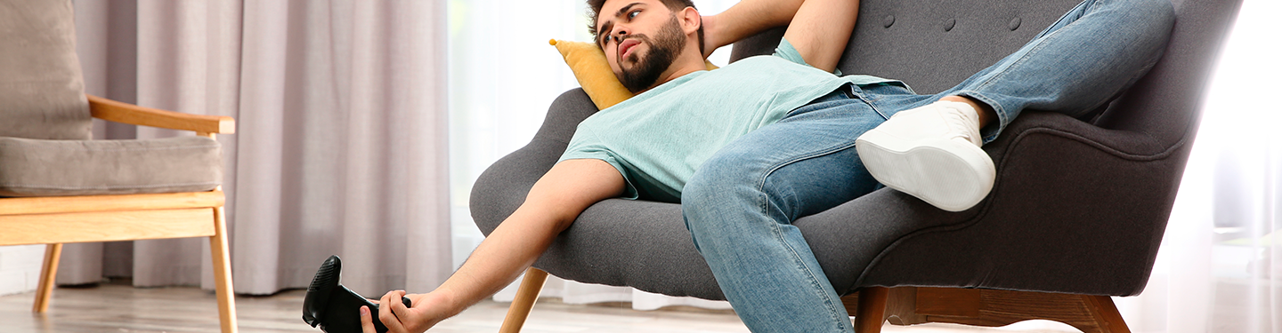 Hombre tirado en el sofá con un mando de play de la mano