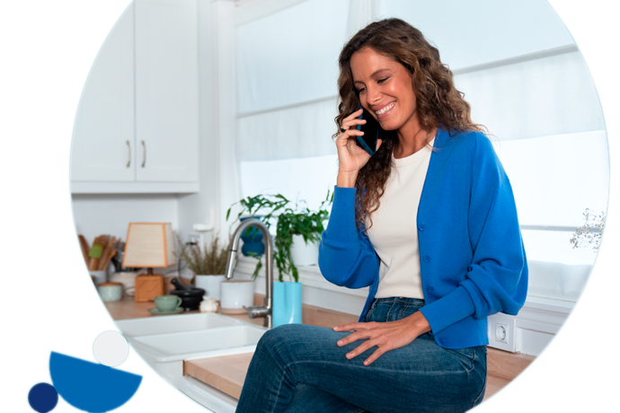 chica sonriente, sentada en la cocina hablando por teléfono