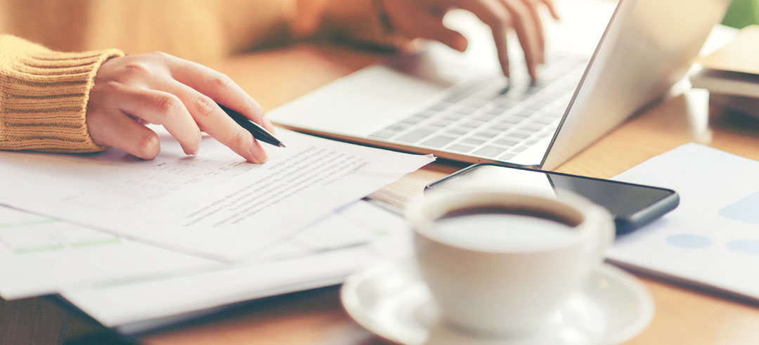 Persona con un ordenador y documentos sobre la mesa